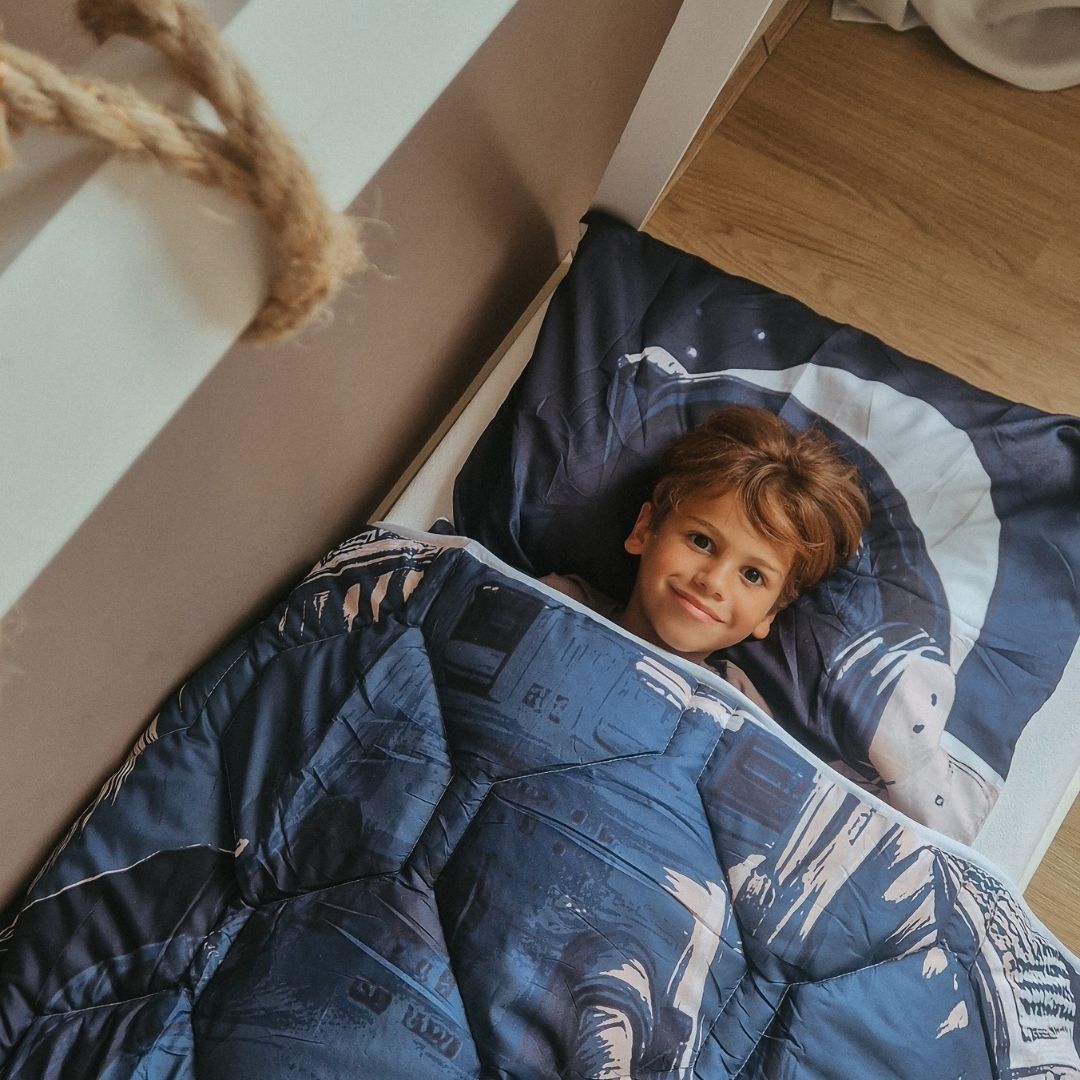Child lying under HappyBed Astronaut kids duvet with matching pillowcase featuring astronaut print