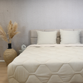 HappyBed Mousseline dekbed in sand color on beige bed with two pillows and decorative vase with pampas grass.