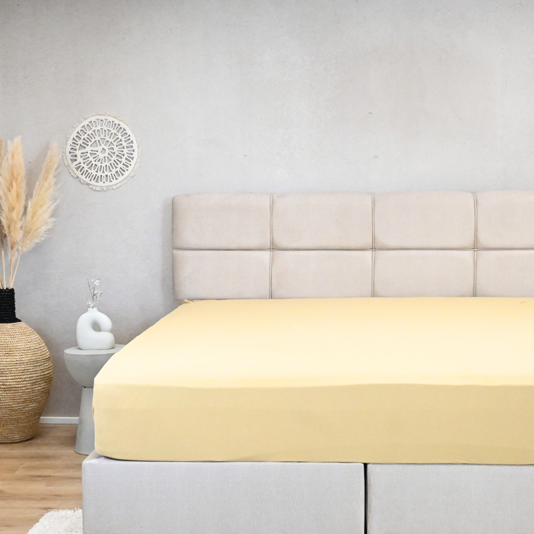 HappyBed premium jersey fitted sheet in ochre yellow, 150gr, on a mattress in a stylish bedroom setting.